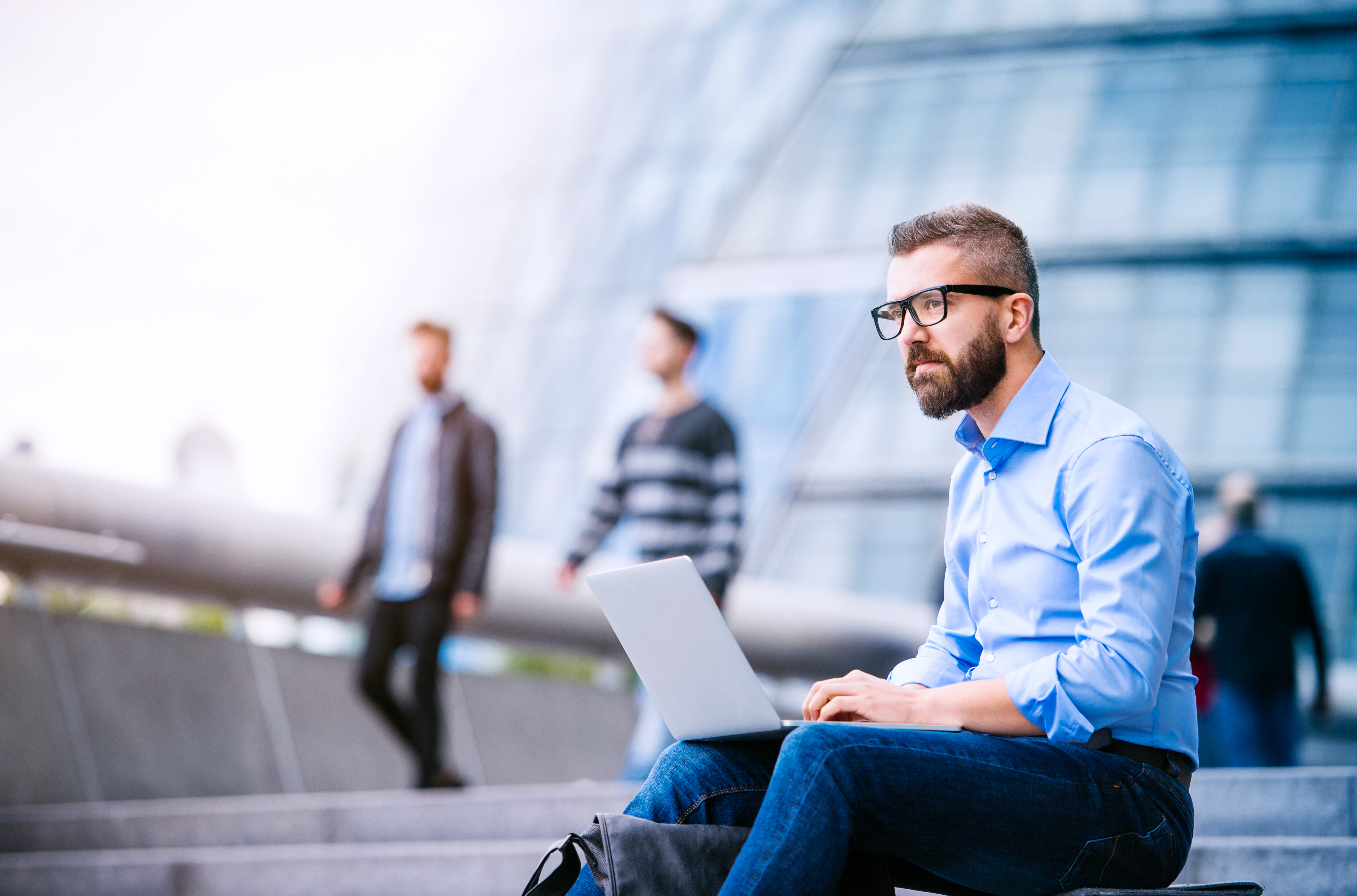hipster-manager-sitting-on-stairs-on-sunny-day-working-on-laptop-london-city-hall-SBI-305194875